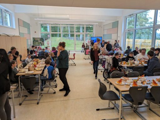 Menschen in einem Speisesaal, Essen an Tischen, entspanntes Ambiente.