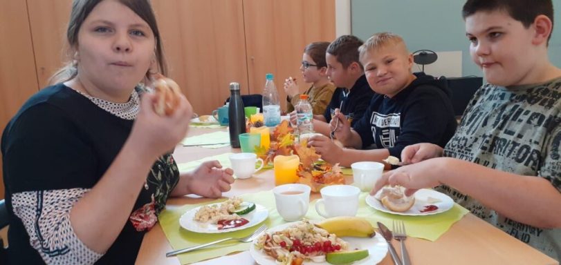 Grupp von Kindern beim Essen an einem Tisch mit Tellern und Getränken.