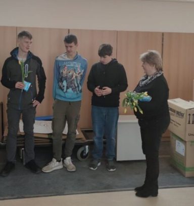 Gruppenszene mit vier Personen, die an einer Präsentation oder Übergabe teilnehmen.