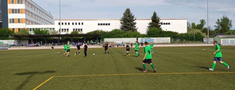 Fußballspiel auf einem Kunstrasenplatz mit Spielern in grünen Trikots.