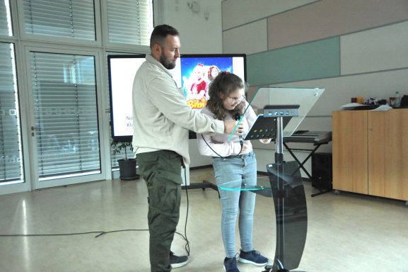 Ein Mann und ein Mädchen stehen vor einem Pult und interagieren mit einem Bildschirm.