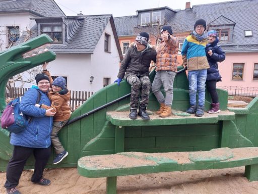 Fünf Kinder und eine Erwachsene spielen auf einem grünen Spielplatzspielgerät.