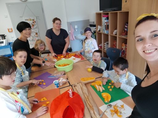 Gruppenszene von Kindern und Erwachsenen beim Obstschneiden und -zubereiten.