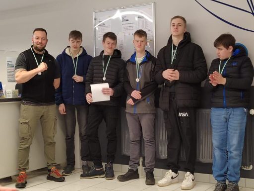 Gruppe von sechs Personen mit Medaillen in einer sportlichen Umgebung.