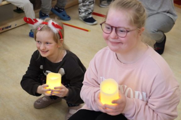 Zwei Mädchen halten leuchtende Kerzen und lächeln dabei freundlich.