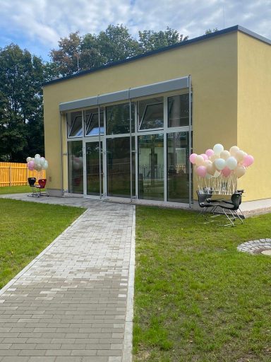 Bunt dekoriertes Gebäude mit großen Fenstern und Luftballons im Freien.