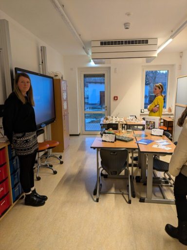 Schulraum mit Lehrern, Tafel und Tischen. Fenster mit Tageslicht.