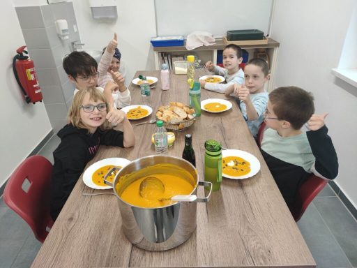 Sechs Kinder sitzen an einem Tisch und essen gemeinsam Karottensuppe.