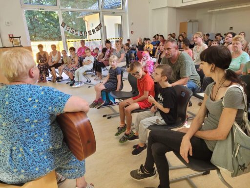 Eine Gruppe von Kindern und Erwachsenen sitzt in einem Raum und hört einer Musikerin zu.