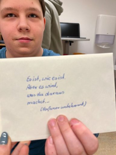 Junge hält ein Blatt Papier mit handgeschriebener Nachricht in der Hand.