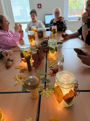 Tischgedeck mit Gläsern, Kerzen und herbstlicher Dekoration, umgeben von Menschen.