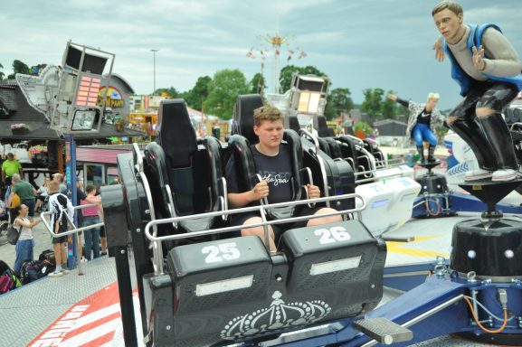 Junger Mann sitzt bereit in einem Fahrgeschäft auf einem Jahrmarkt. Menschen im Hintergrund.