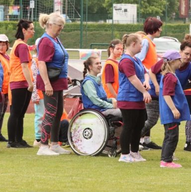 Kinder und Jugendliche in Sportbekleidung, einige tragen Westen, auf einem Sportplatz.