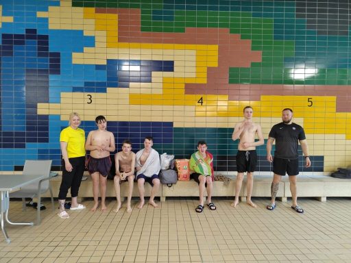 Gruppe von Personen am Schwimmbad mit bunten Fliesen im Hintergrund.