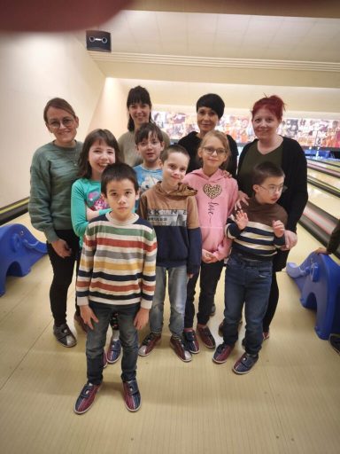 Eine Gruppe von Kindern und Erwachsenen in einer Bowlingbahn, lächelnd und freundlich.