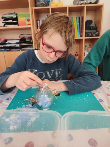 Ein Kind bastelt an einer transparenten Kugel mit blauen und weißen Materialien.