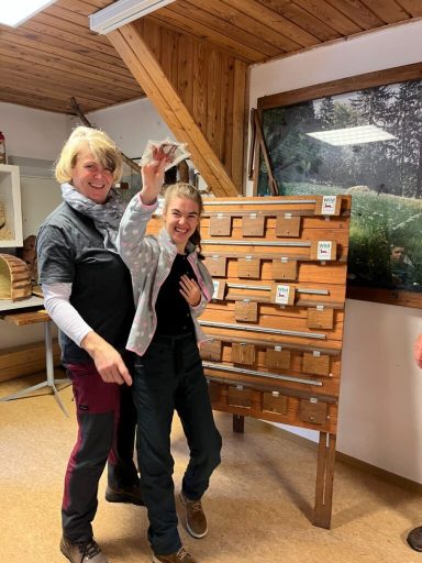 Zwei Frauen posieren vor einem Holztresen mit Schubladen in einem Raum.