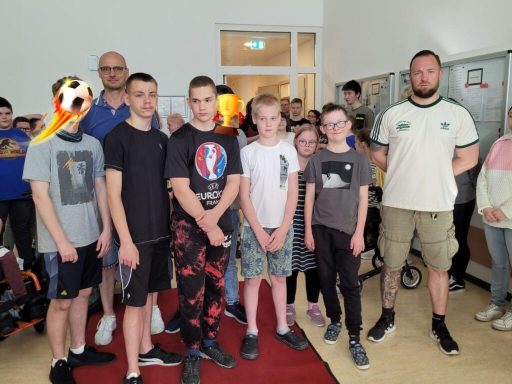 Gruppe von Jugendlichen und Erwachsenen in einem Raum, einige lächeln, andere schauen direkt.