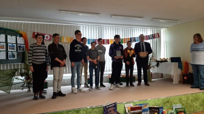 Gruppenevent mit mehreren Personen, die auf einer Bühne oder in einem Raum stehen, feierliche Stimmung.