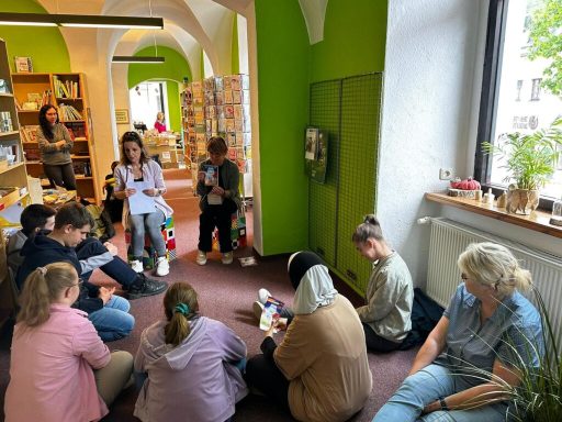 Kinder und Erwachsene sitzen in einem hellen Raum mit Büchern und Spielsachen.