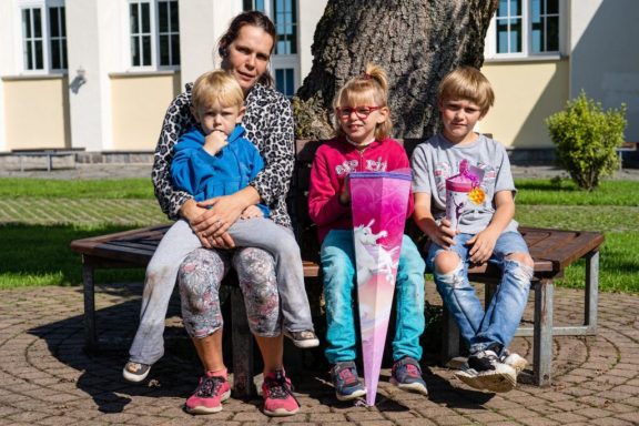 Frau mit drei Kindern, die auf einer Bank sitzen, zwei Kinder halten Schultüten.