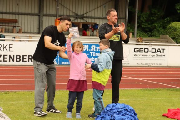 Ein Junge und ein Mädchen erhalten Preise, umgeben von jubelnden Erwachsenen.