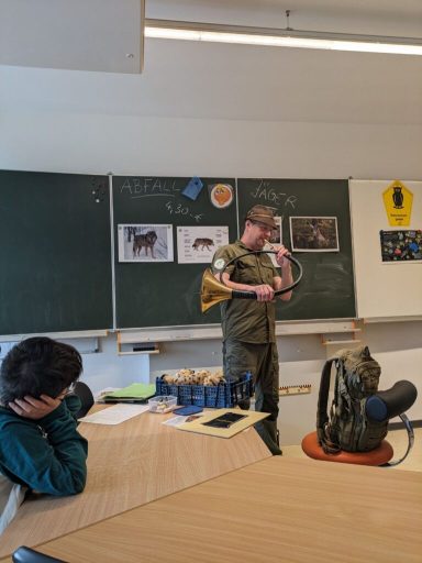 Ein Mann in Uniform spricht vor einer Tafel, während ein Jugendlicher zuhört.