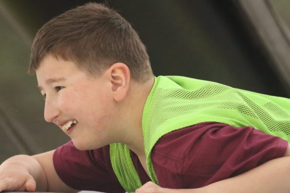 Junger Junge in grünem Sicherheitsweste, lächelnd und aktiv.