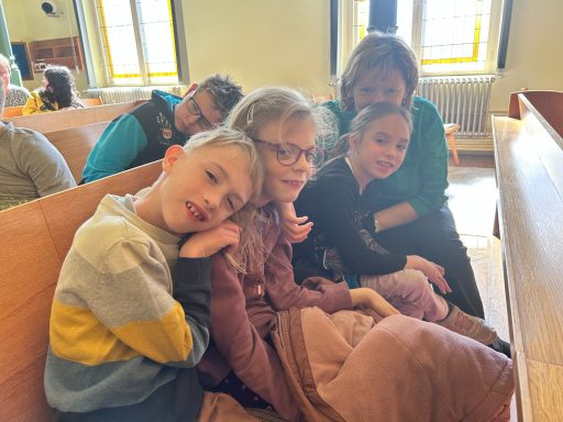 Fünf Kinder und Erwachsene sitzen in einer Kirche und lächeln in die Kamera.