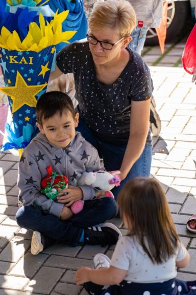 Eine Frau sitzt mit einem Jungen und einem kleinen Mädchen auf dem Boden, umgeben von bunten Dekorationen.