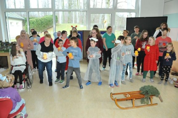 Gruppenvorführung von Kindern in Kostümen in einem hellen Raum mit Zuschauer.
