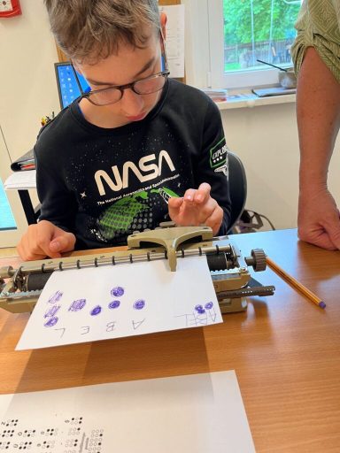 Ein Junge mit Brille bedient eine Schreibmaschine und macht Druck auf ein Blatt Papier.