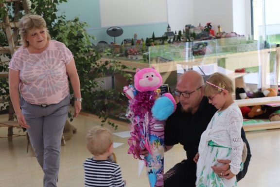 Eine Person mit einer Puppe interagiert mit zwei Kindern, während eine Frau zuschaut.