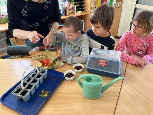 Kinder pflanzen Samen in Töpfen, während sie von einer Erwachsenen angeleitet werden.
