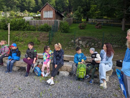 Gruppe von Kindern und Erwachsenen sitzt auf einer Bank in der Natur.
