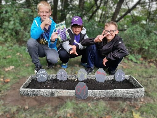 Drei Kinder posieren am Steinbeet mit bemalten Steinen im Hintergrund.