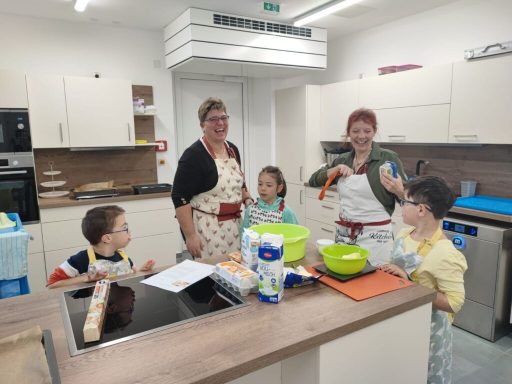 Familie kocht zusammen in einer modernen Küche, alle lächeln und arbeiten an einem Rezept.