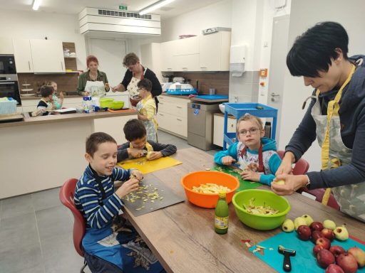 Kinder und Erwachsene bereiten in einer Küche gemeinsam Obst in bunten Schalen zu.