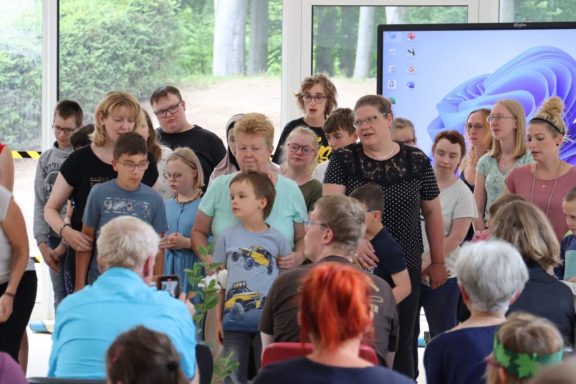 Eine Gruppe von Menschen, darunter Kinder, singt oder tritt auf einer Veranstaltung auf.