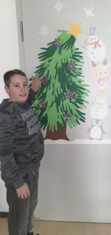 Ein Junge steht neben einem dekorierten Weihnachtsbaum und einem Schneemann.