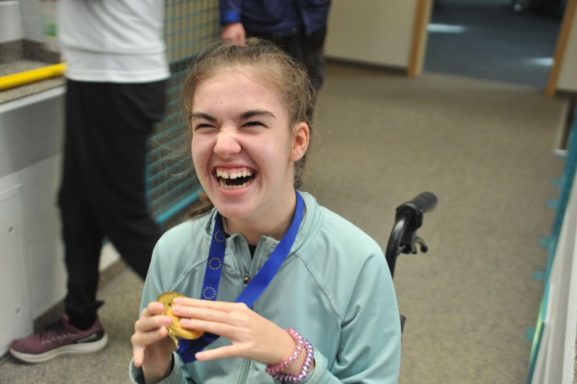 Ein glückliches Mädchen mit Medaille, das ein Lächeln zeigt und einen Keks hält.