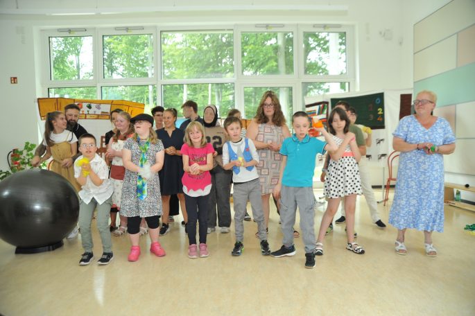Gruppe von Kindern und Erwachsenen, die in einem hellen Raum gemeinsam posieren.