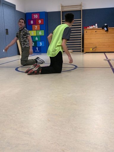 Zwei Kinder knien in einer Turnhalle, eines trägt eine leuchtend grüne Weste.