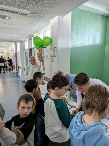 Gruppe von Kindern und Erwachsenen in einem Raum, einige halten grüne Luftballons.