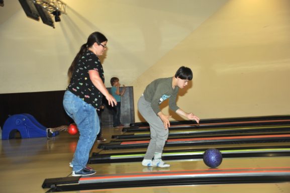 Ein Junge bereitet sich beim Bowlen vor, während eine Frau ihn unterstützt.