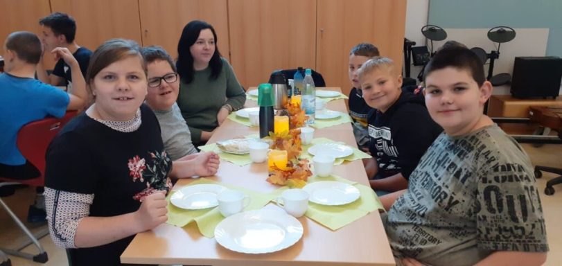 Sechs Kinder am Tisch mit gedeckten Tellern und Getränken, fröhliche Atmosphäre.