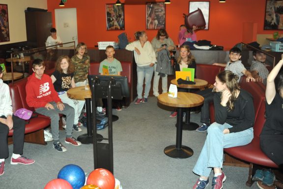 Gruppe von Jugendlichen sitzt in einem Café, einige sprechen, andere schauen aufmerksam zu.