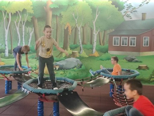 Kinder spielen auf einem Spielplatz mit Trampolinen vor einer Waldlandschaft.