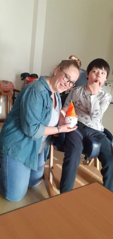 Frau mit einer orangefarbenen Figur, neben einem Jungen, der nachdenklich wirkt.