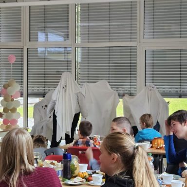Weiße T-Shirts hängen hinter einer Gruppe von Menschen in einer Cafeteria.